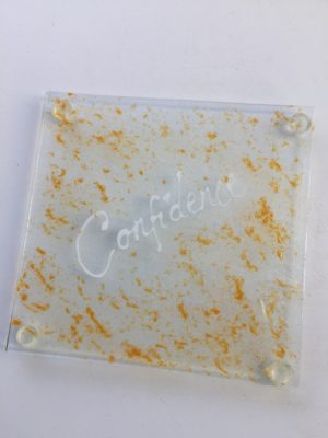 Confidence Written in white writing on an orange coloured piece of glass